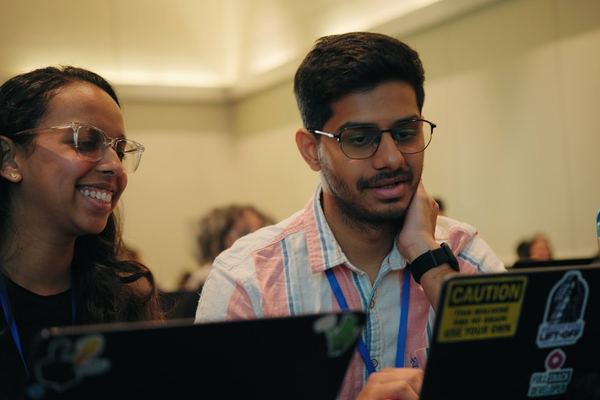 Two attendees smile while working together on their laptops