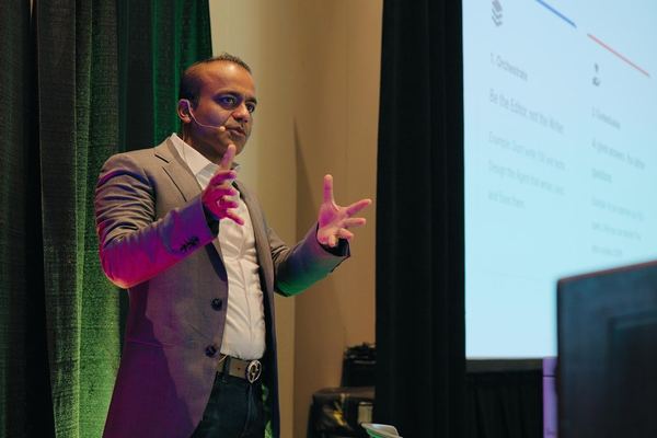 A speaker wearing a headset microphone gestures while presenting on stage